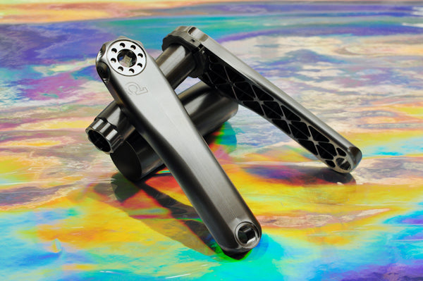 Sturdy machined titanium crankset, both arms, on an iridescent background