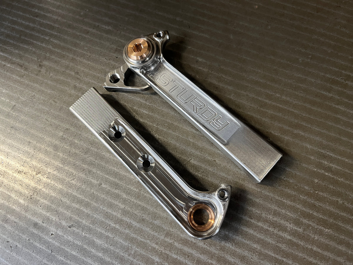 Two machined titanium rear dropouts laid side by side on a steel bench