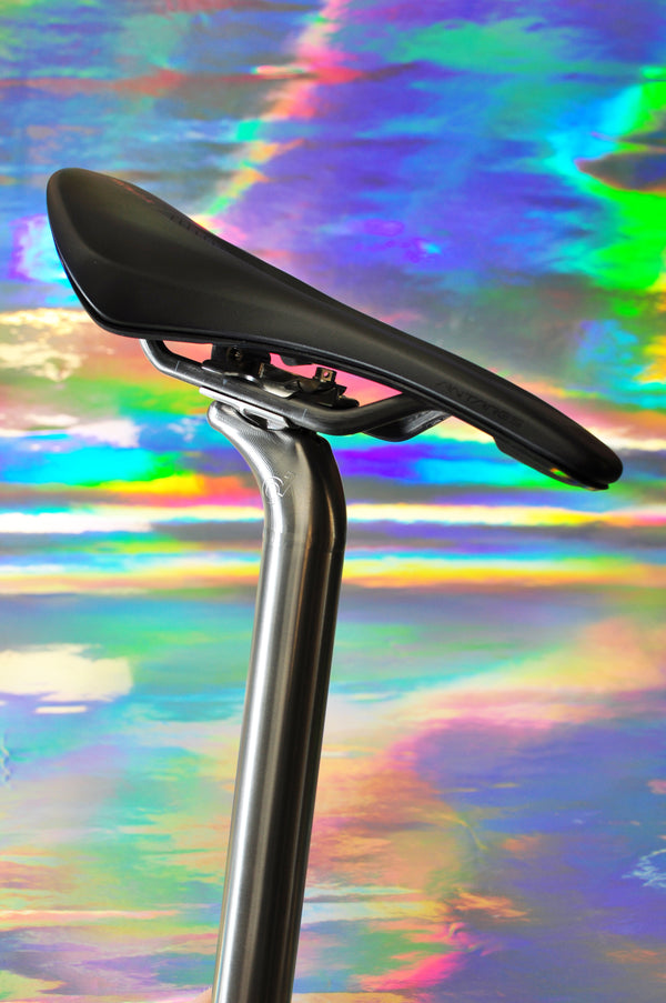 Sturdy titanium seatpost with a saddle fitted, on an iridescent background