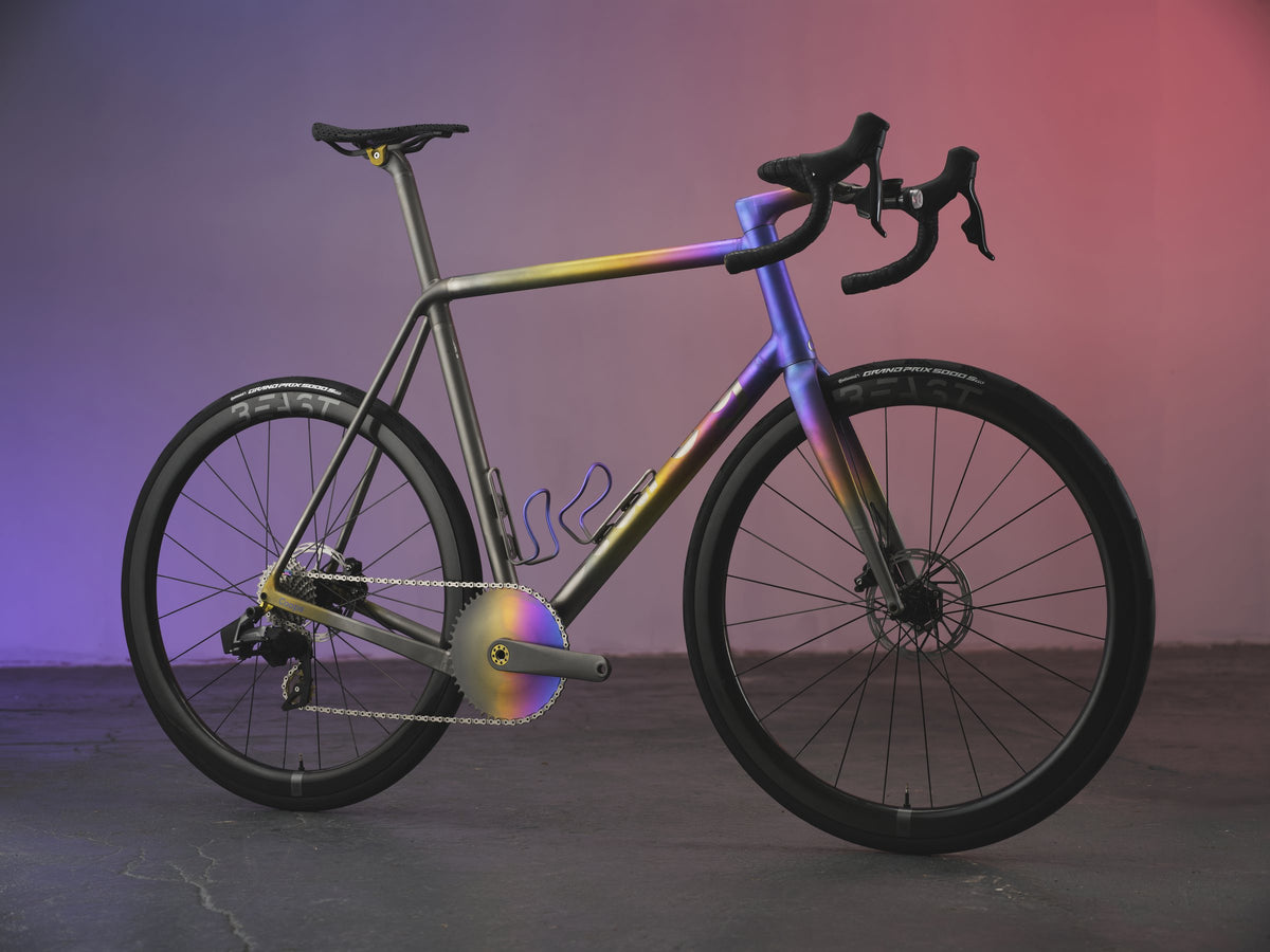 Road bike with yellow, purple and blue anodised fade over titanium, on a pink and purple backdrop