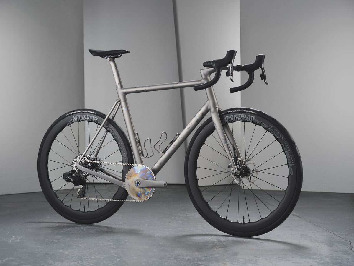 Titanium road bike with mottled rainbow anodised graphics and chainring in a grey studio