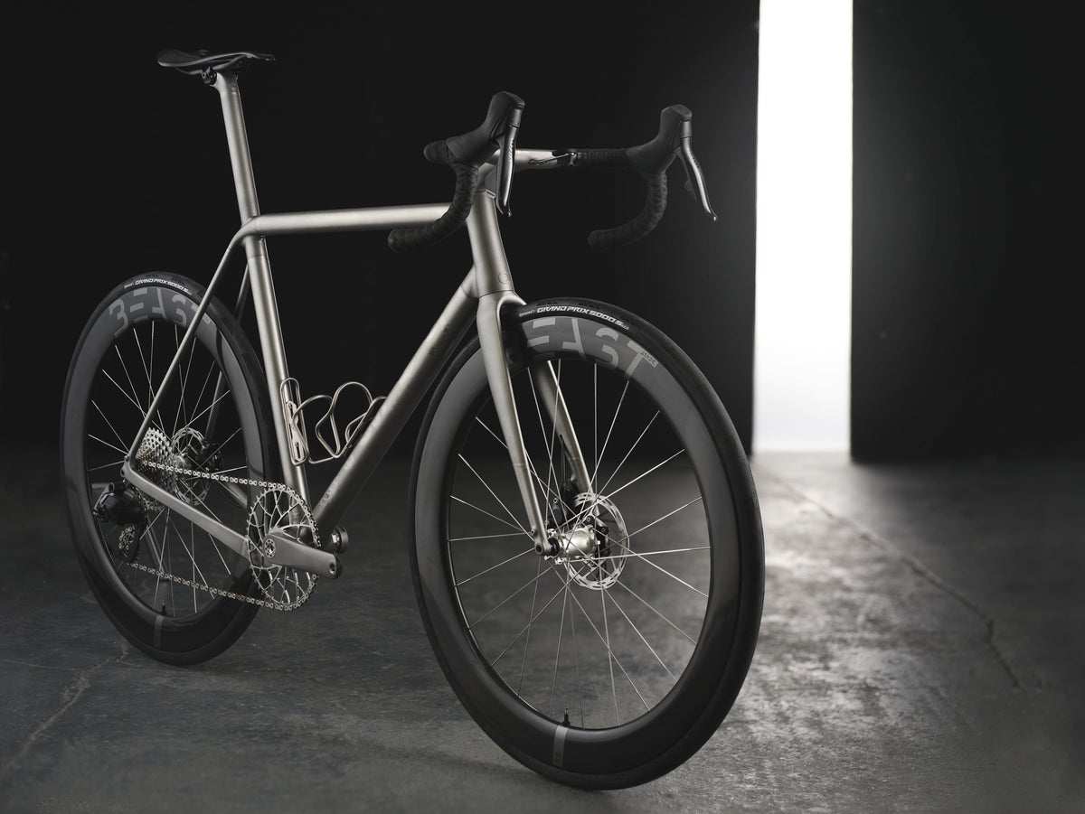 Titanium road bike with deep-section carbon wheels lit by a shaft of light in a dark studio