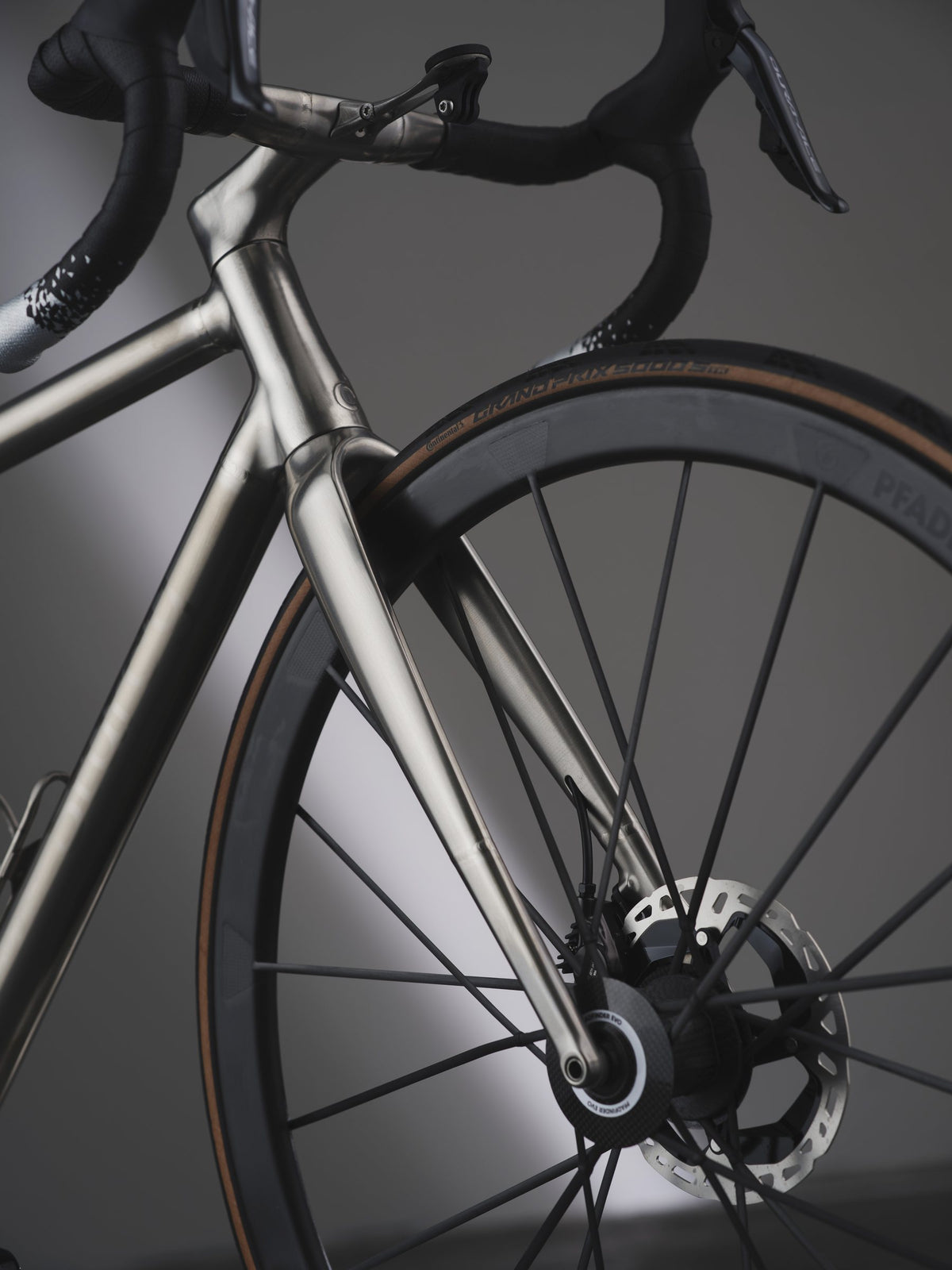 Titanium head tube and fork with tan-wall tyre and deep carbon wheel in dramatic studio light