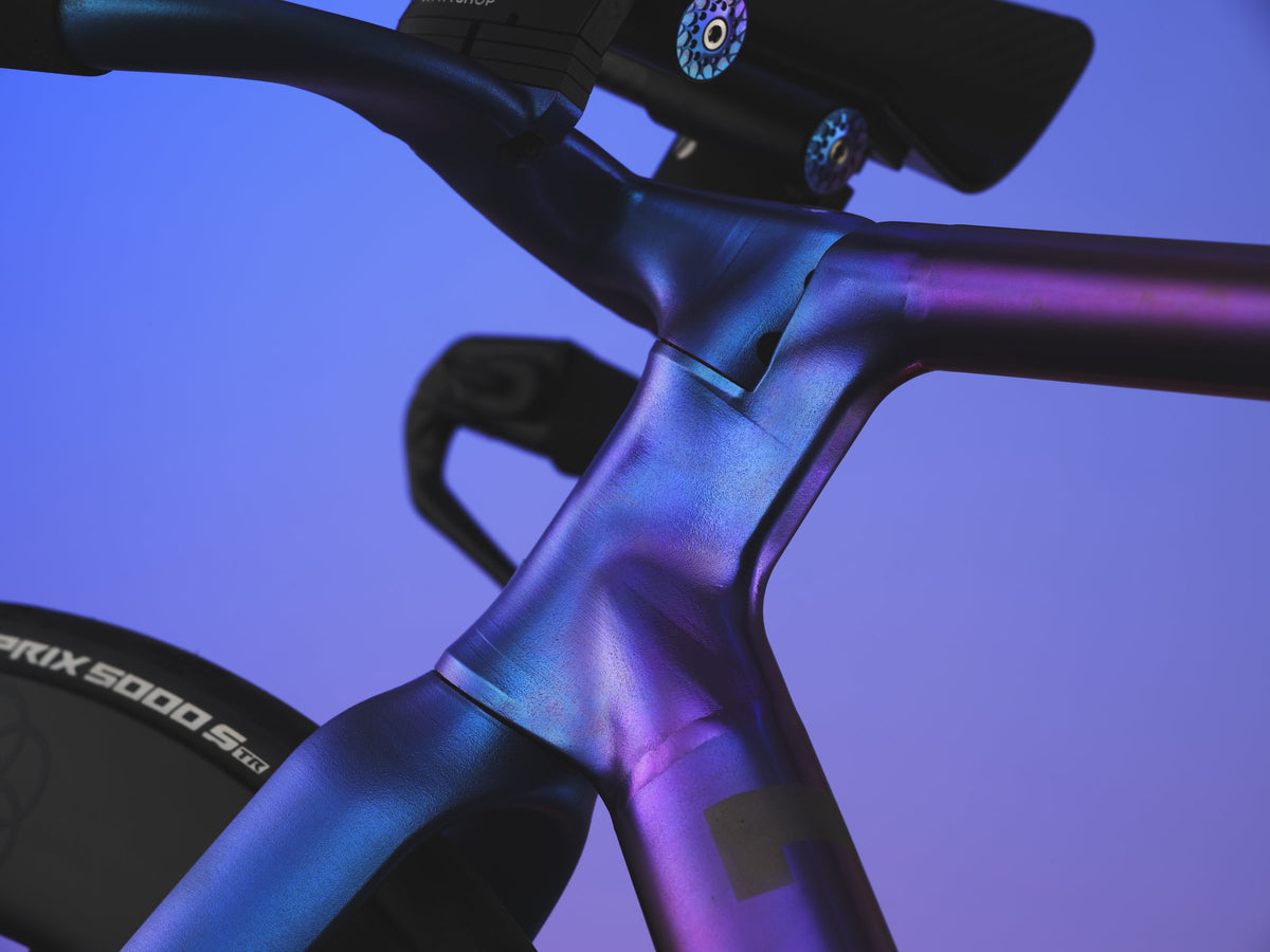 Blue-purple anodised titanium front end of a time trial bike with aero extensions, purple backdrop