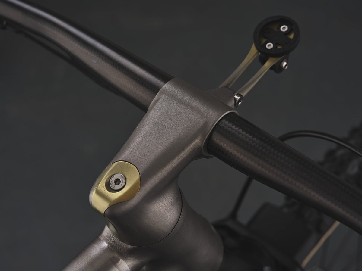 Titanium stem with gold top cap, carbon flat handlebar and titanium computer mount on dark background