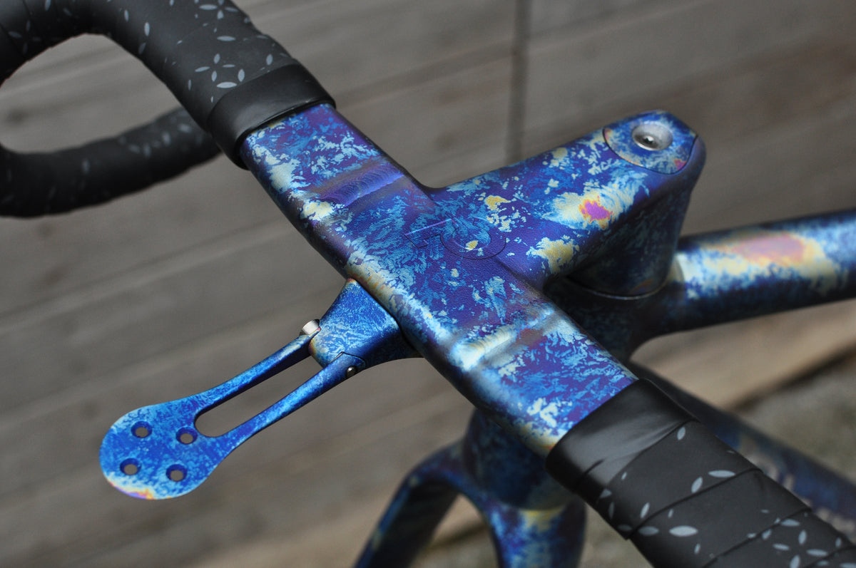 Integrated titanium handlebar and computer mount with a mottled blue and gold anodised finish