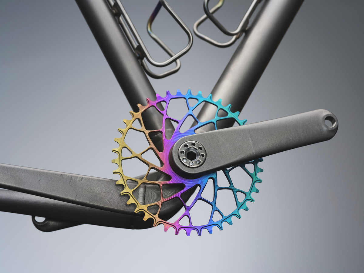 Rainbow anodised chainring on a titanium crank arm and frame, studio close-up