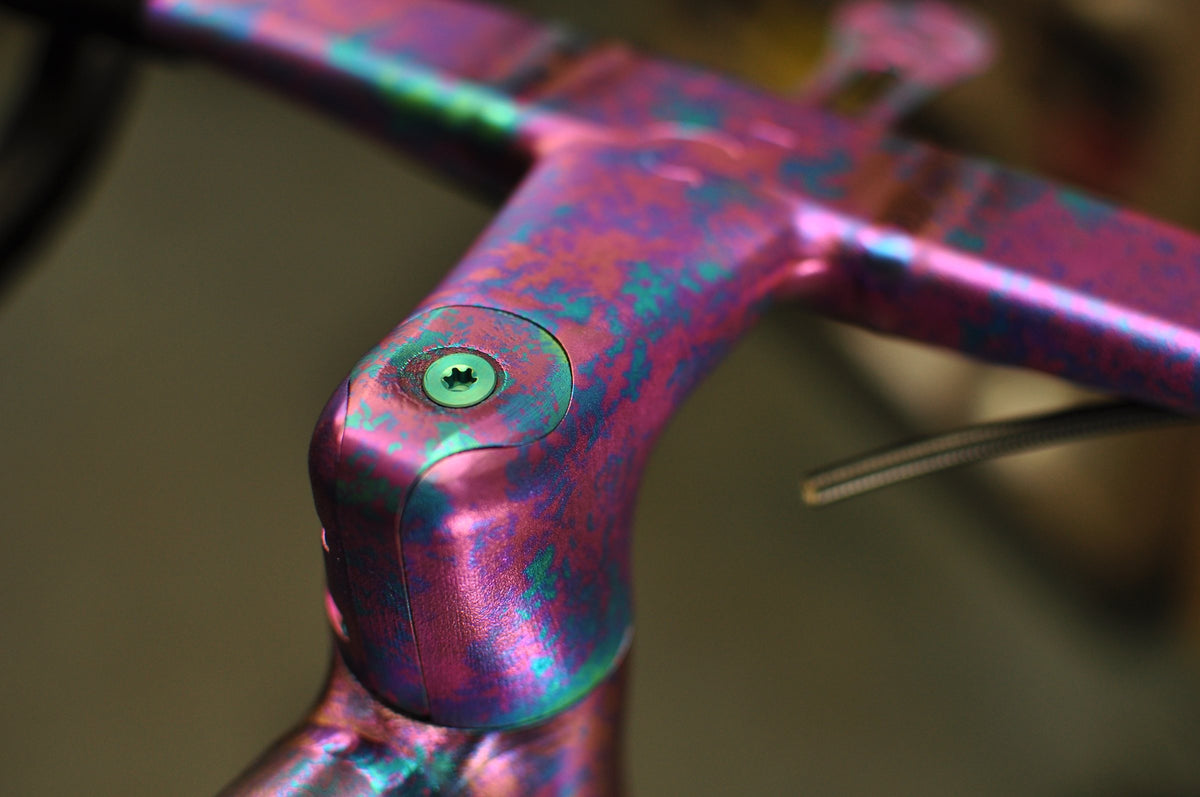Integrated stem and handlebar with a mottled pink, purple and teal anodised titanium finish