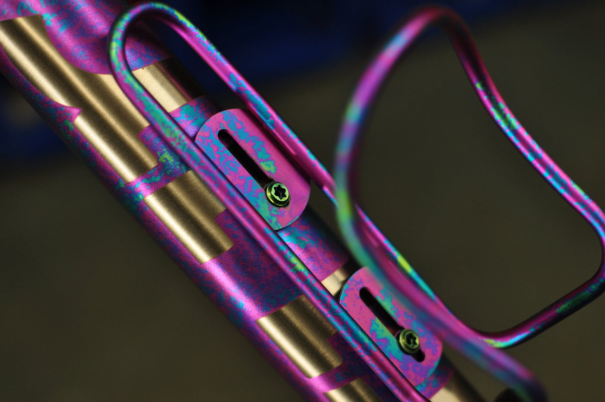 Down tube and matching bottle cage in mottled pink and teal anodising over bare titanium