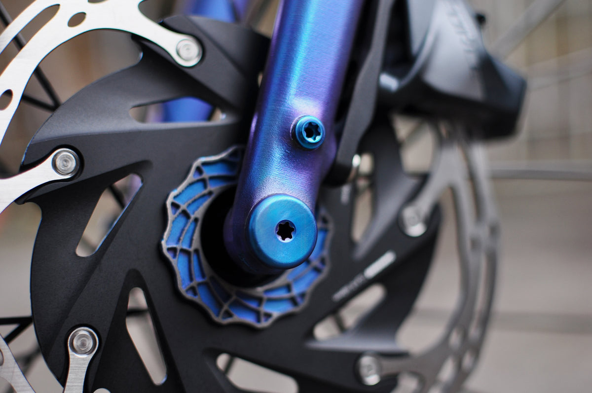 Blue-to-purple anodised fork leg with blue thru-axle and web-pattern disc rotor spider