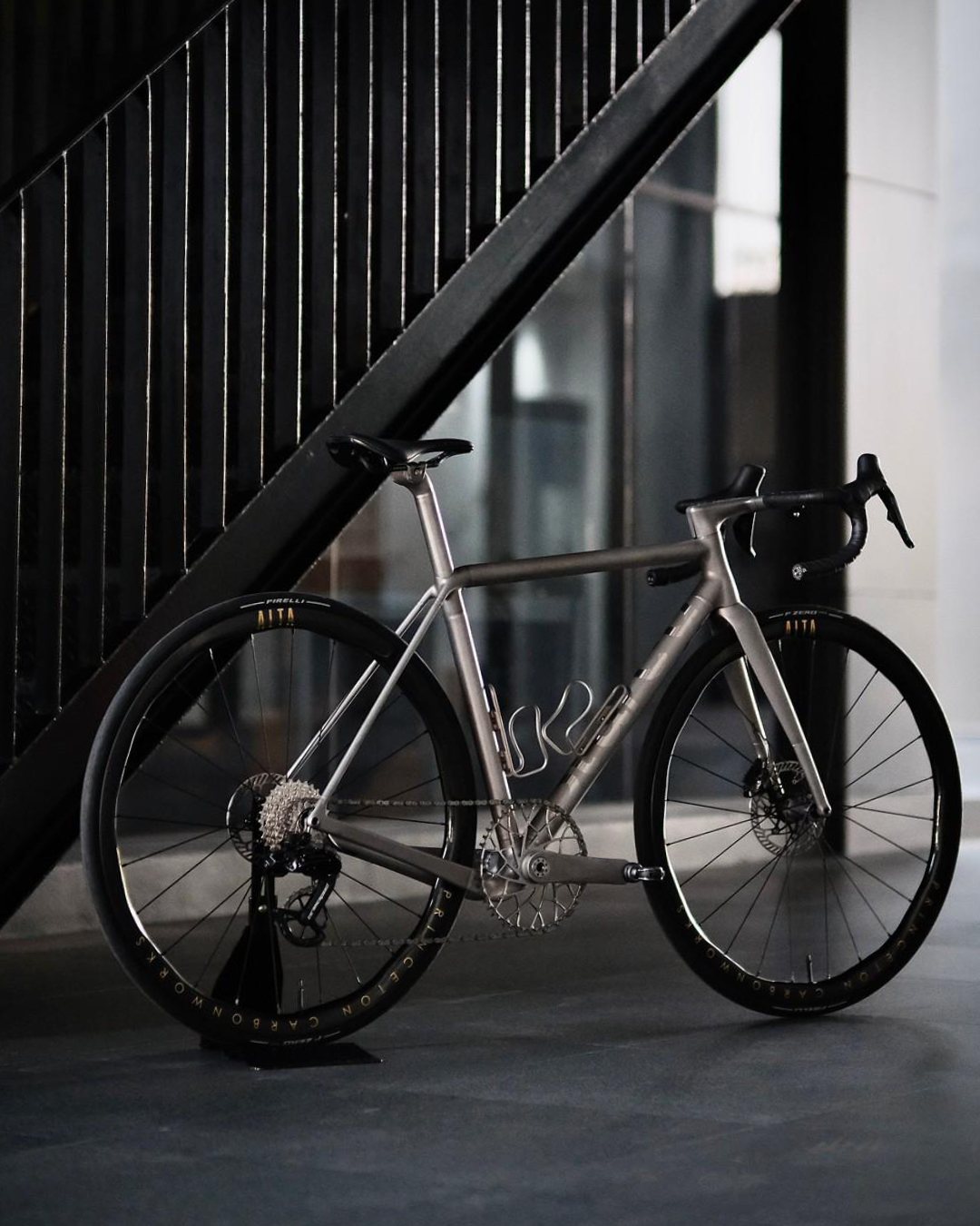 Titanium road bike with deep carbon wheels parked beneath a black metal staircase