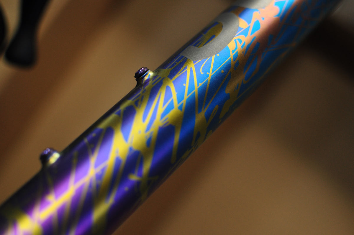 Titanium tube with blue, purple and gold anodised splatter paint and a Sturdy logo