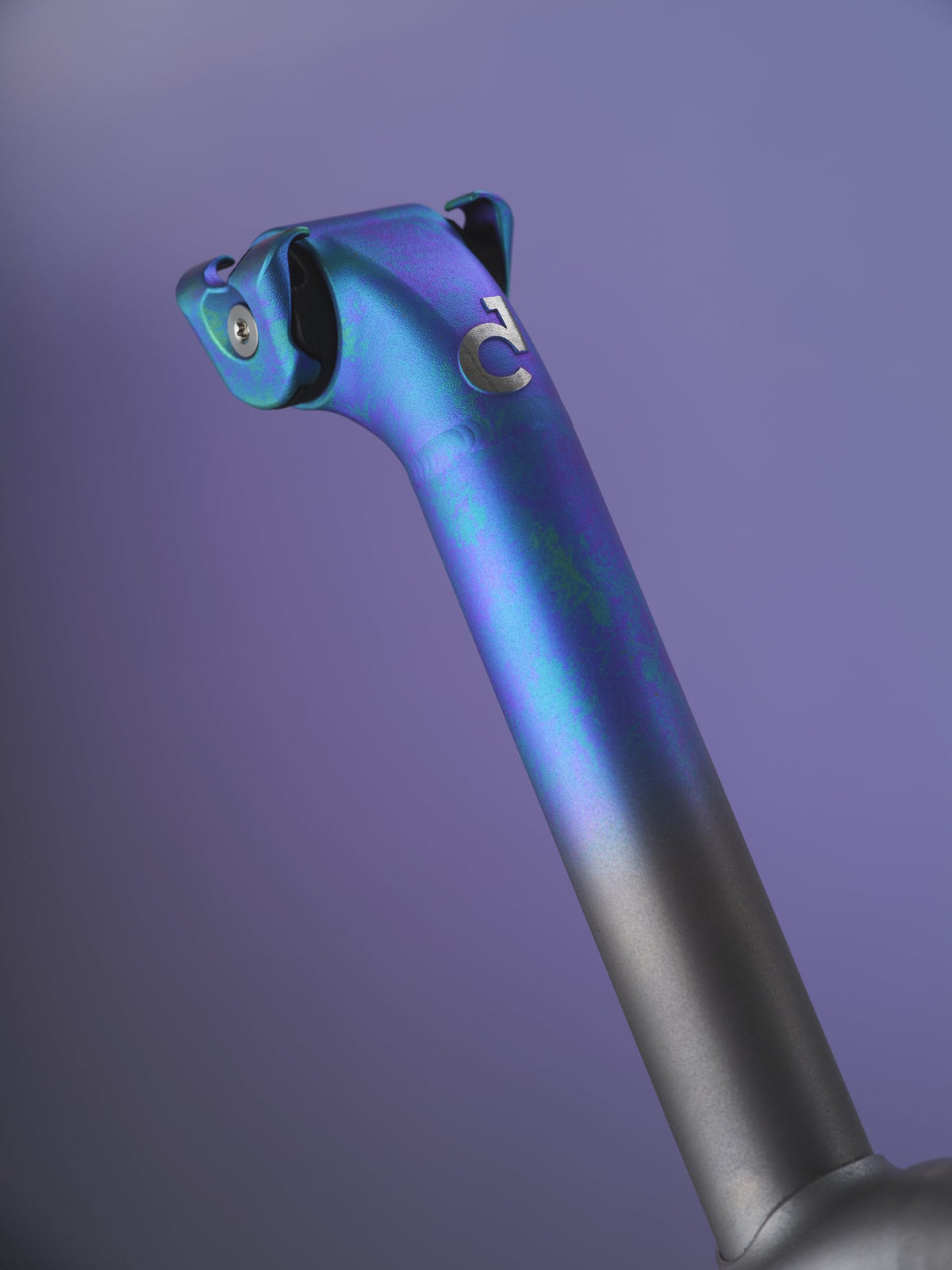 Seatpost head with blue-purple oil-slick anodising fading to grey titanium, on a purple backdrop