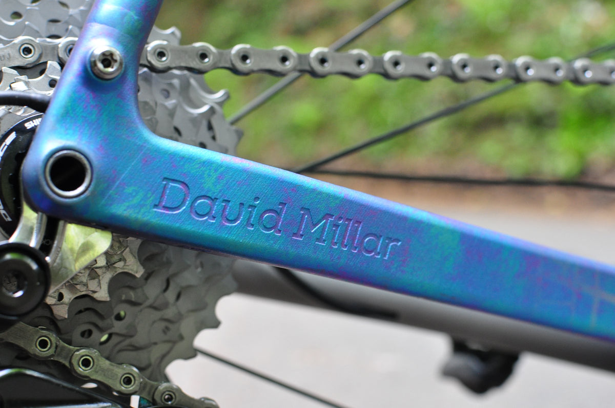 Blue-purple oil-slick anodised titanium chainstay with an engraved name beside the cassette