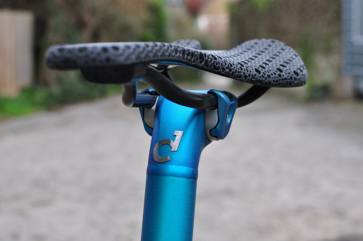 Blue anodised titanium seatpost with etched logo under a black lattice saddle