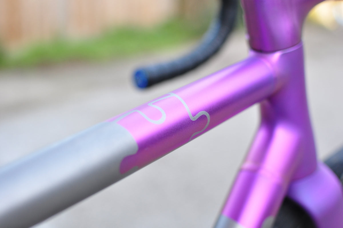 Top tube with a pink-purple anodised section and jigsaw-edged mask meeting bare titanium