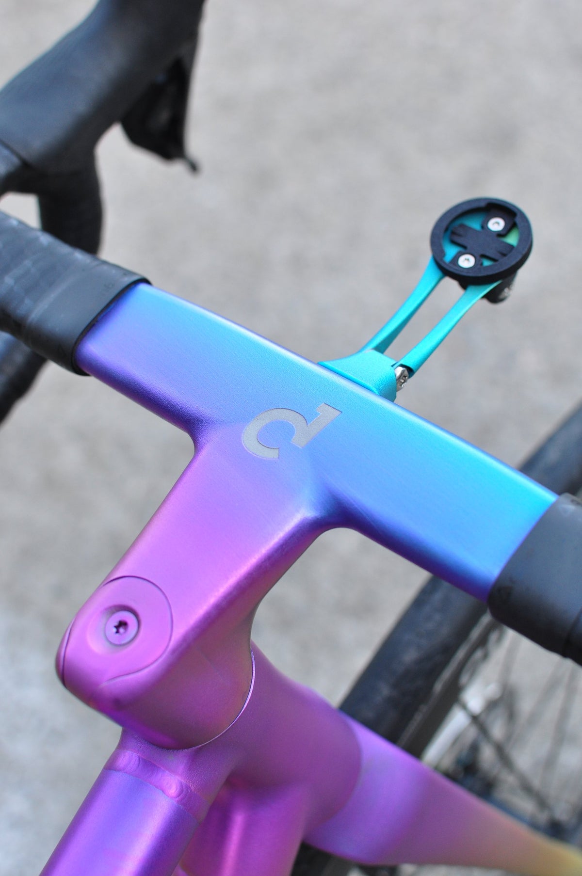 Integrated handlebar in a purple-to-teal anodised fade with etched logo and teal computer mount