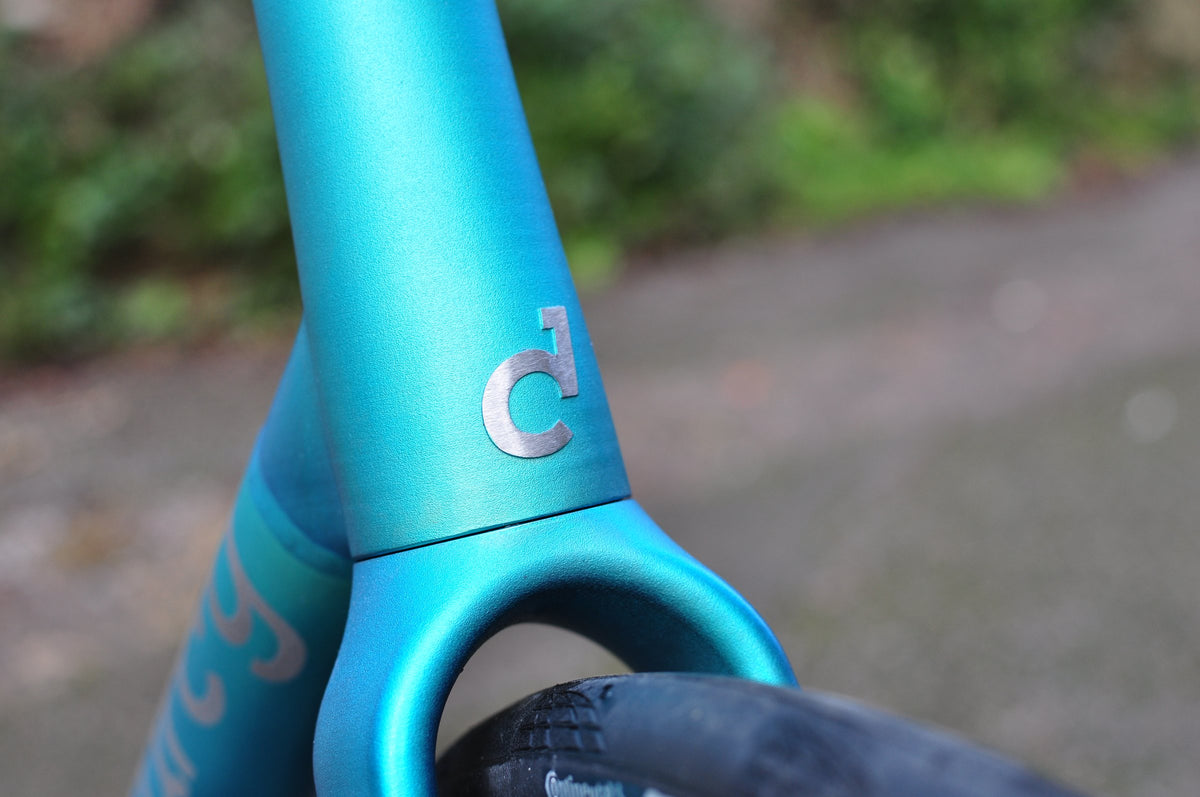 Head tube and fork crown in teal anodised finish with a silver logo badge