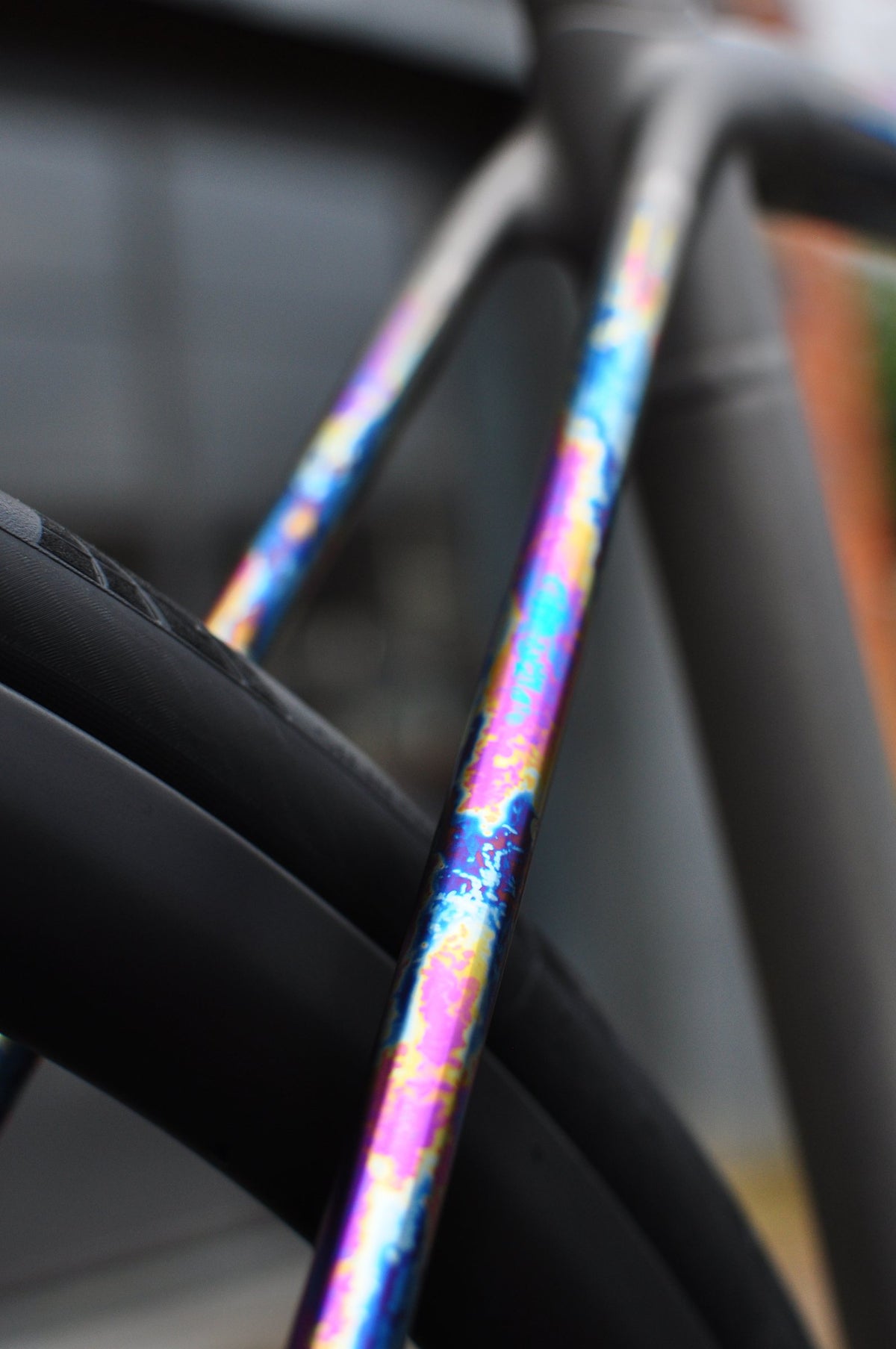 Titanium seat stays with rainbow anodised splatter finish over a dark wheel, close-up