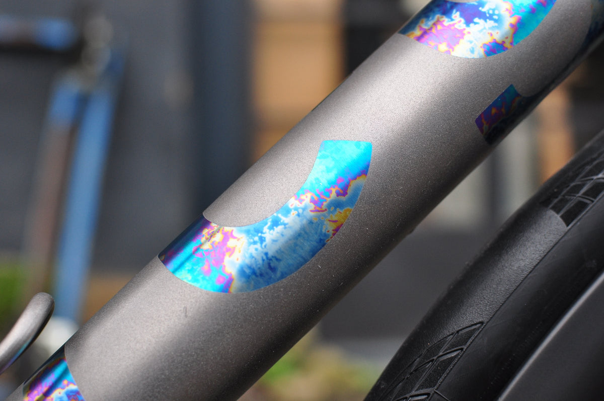 Shot-peened titanium tube with rainbow anodised crescent shapes in a repeating pattern
