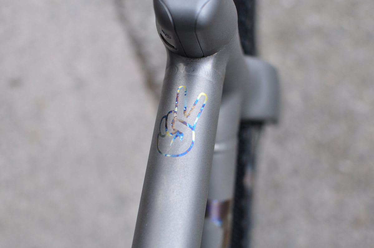Grey titanium head tube with rainbow anodised peace sign hand logo, integrated stem above