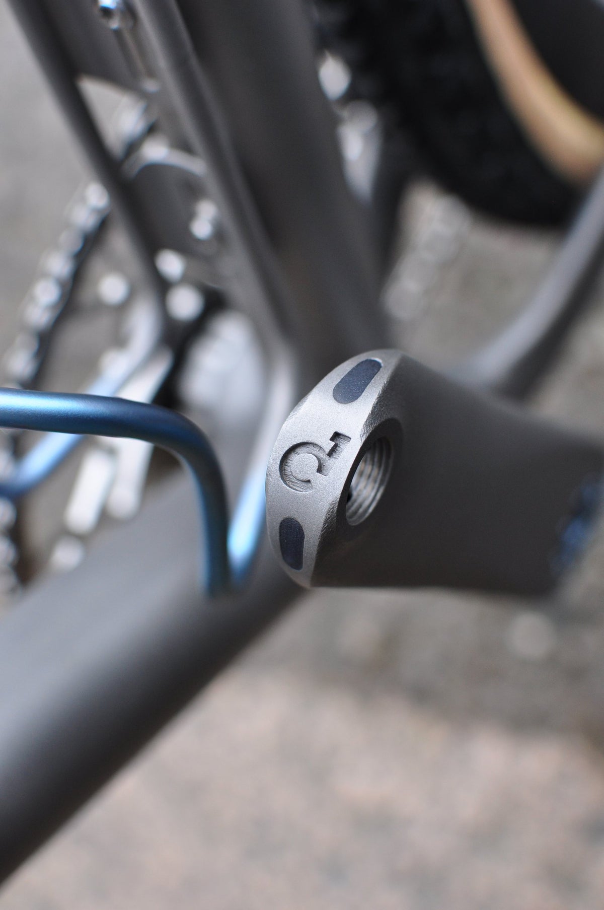 Machined titanium frame end with engraved logo, with a blue anodised titanium bottle cage in soft focus