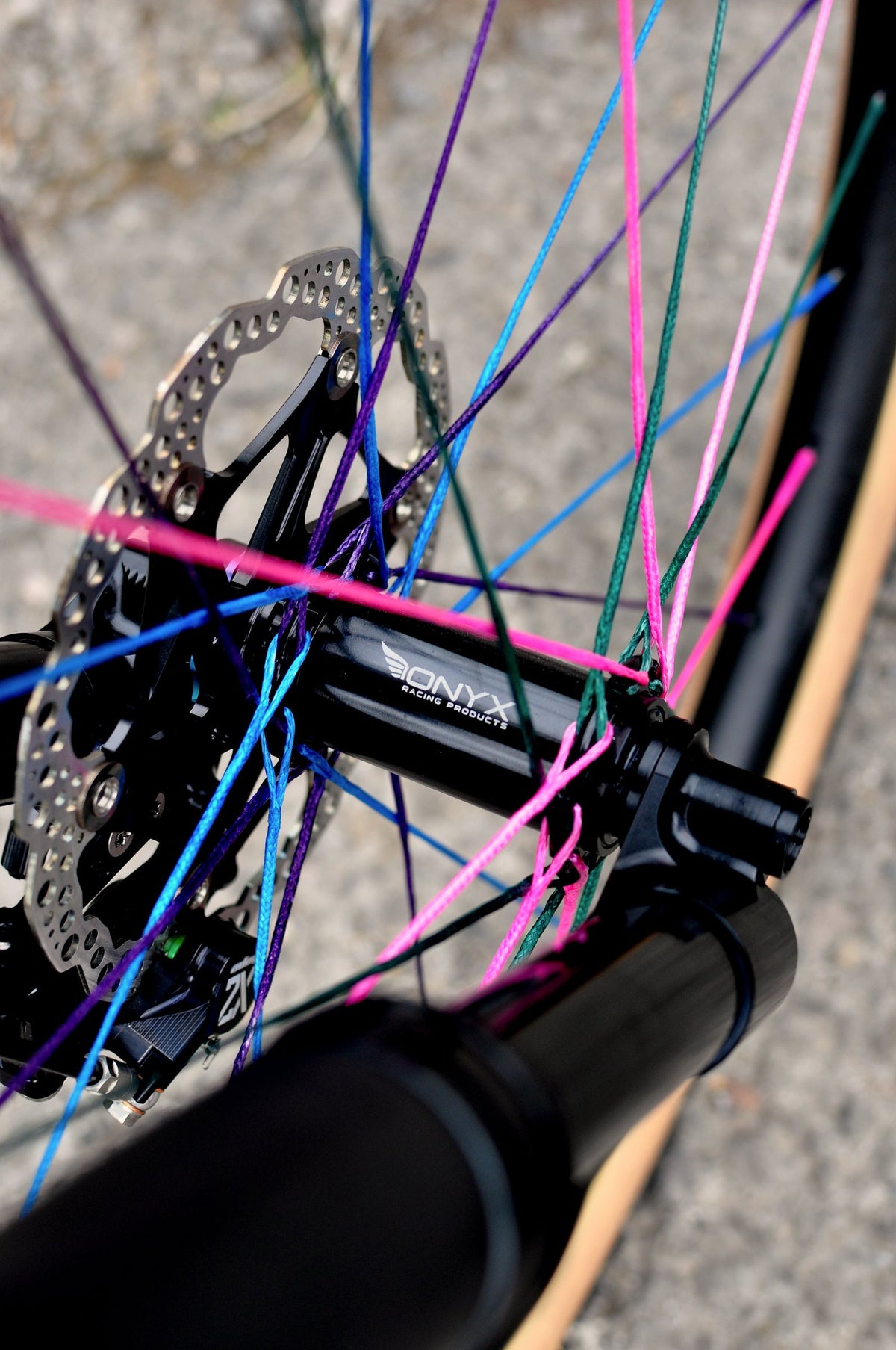 Front hub and disc rotor laced with pink, blue, purple and green textile spokes