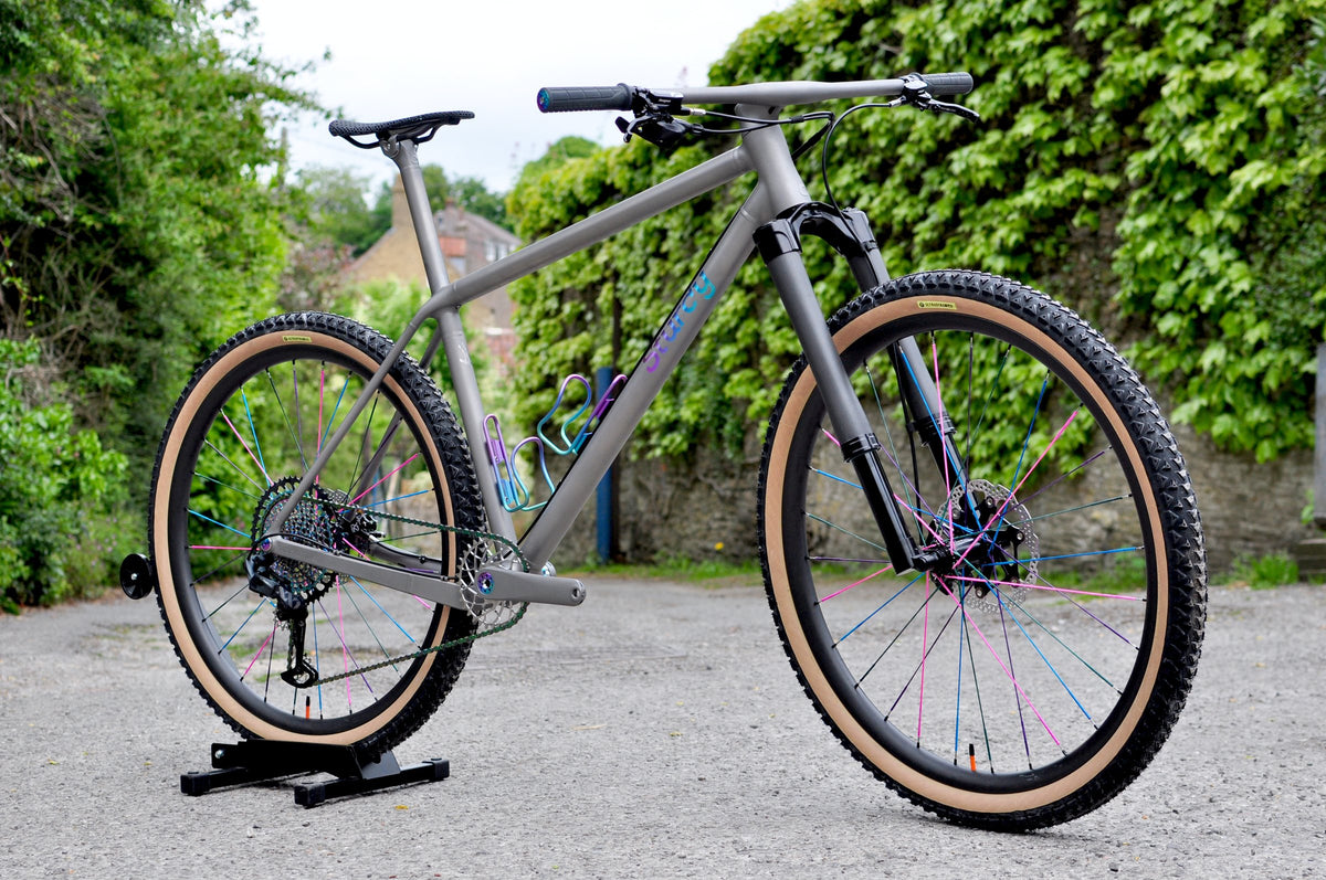 Titanium hardtail mountain bike with rainbow anodised logo and cages, multicoloured spokes and tan-wall tyres