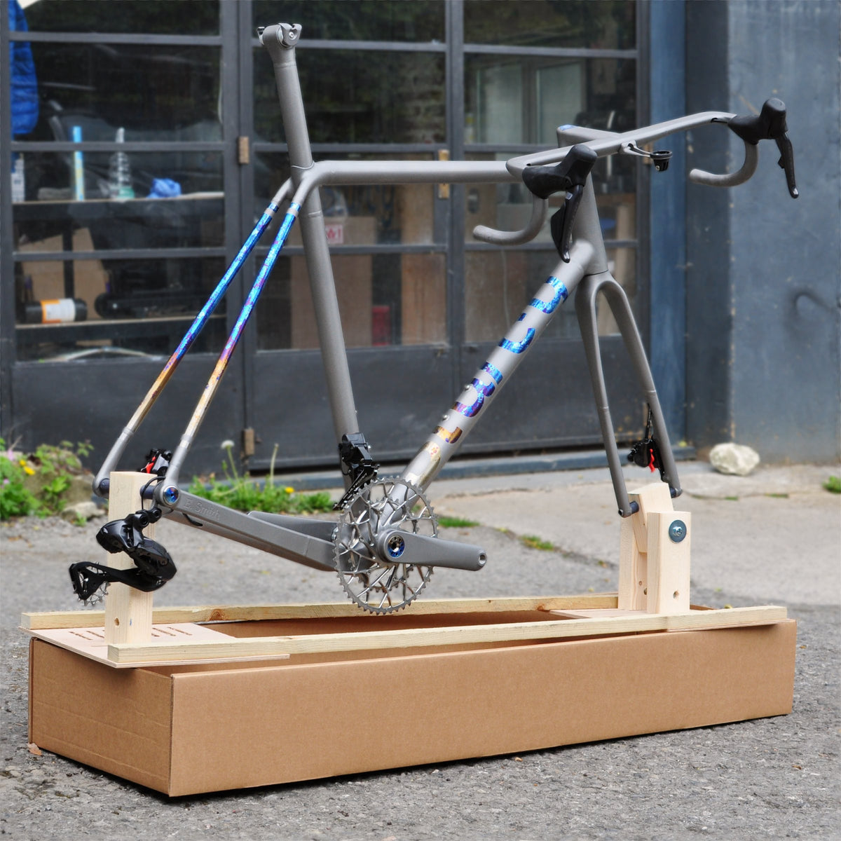 Titanium road frameset with rainbow anodised logo and seatstays on a wooden jig over a shipping box