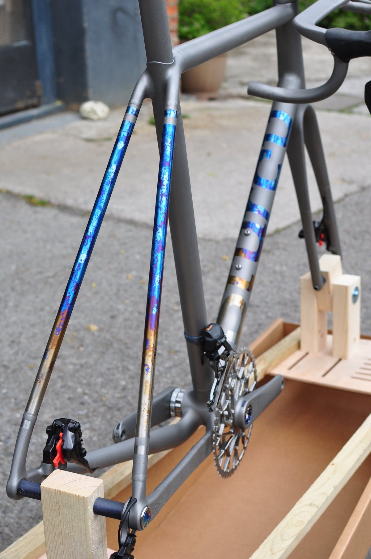 Titanium seatstays and down tube logo with blue and gold anodised splatter, frame in a wooden packing jig