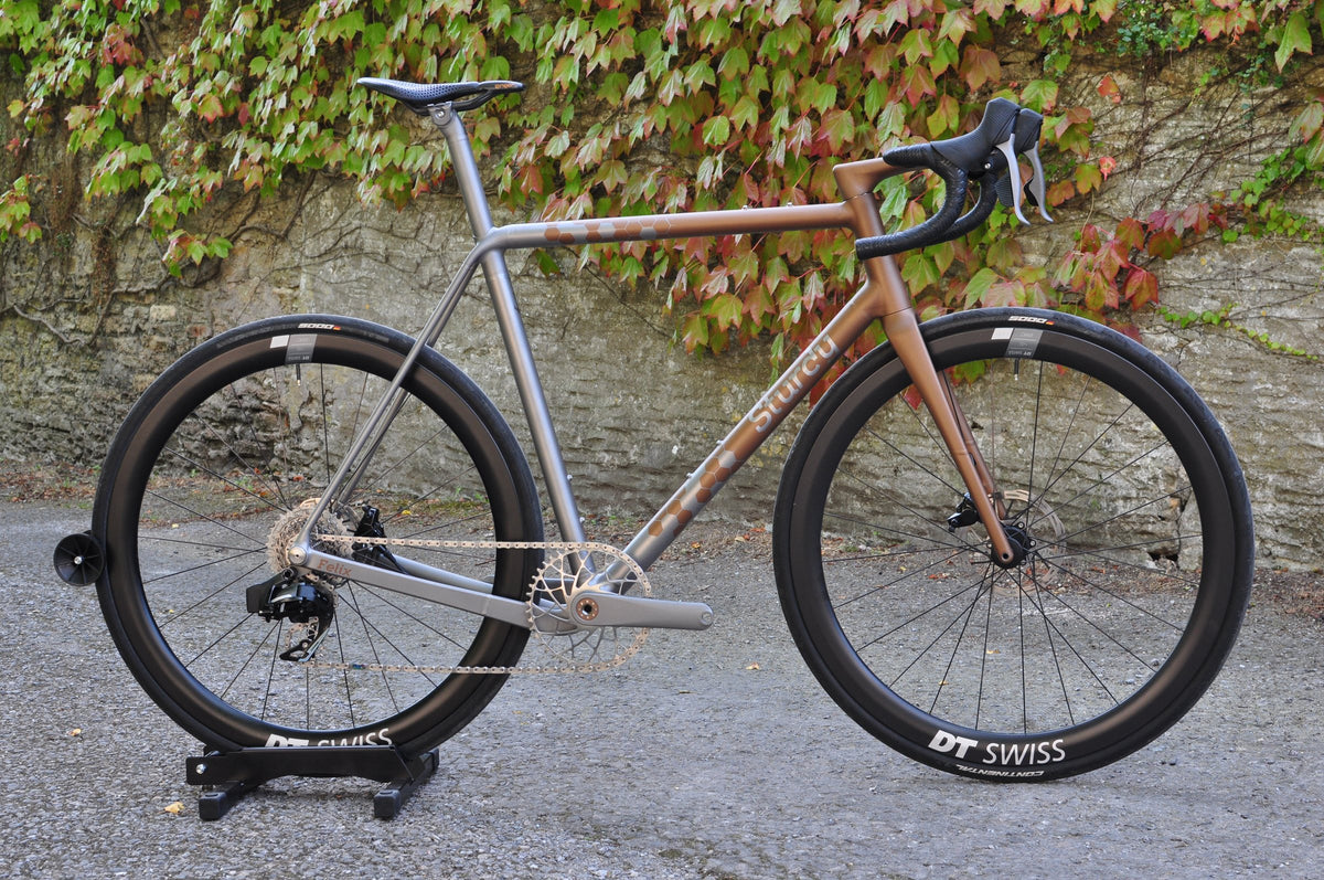 Titanium road bike with copper fade paint and Sturdy logo in front of an ivy-covered stone wall