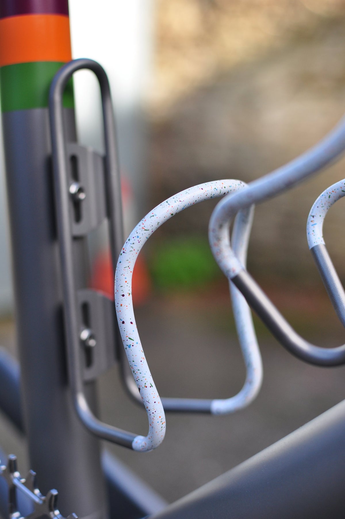 White bottle cage with multicoloured speckles on a grey frame with coloured stripe bands