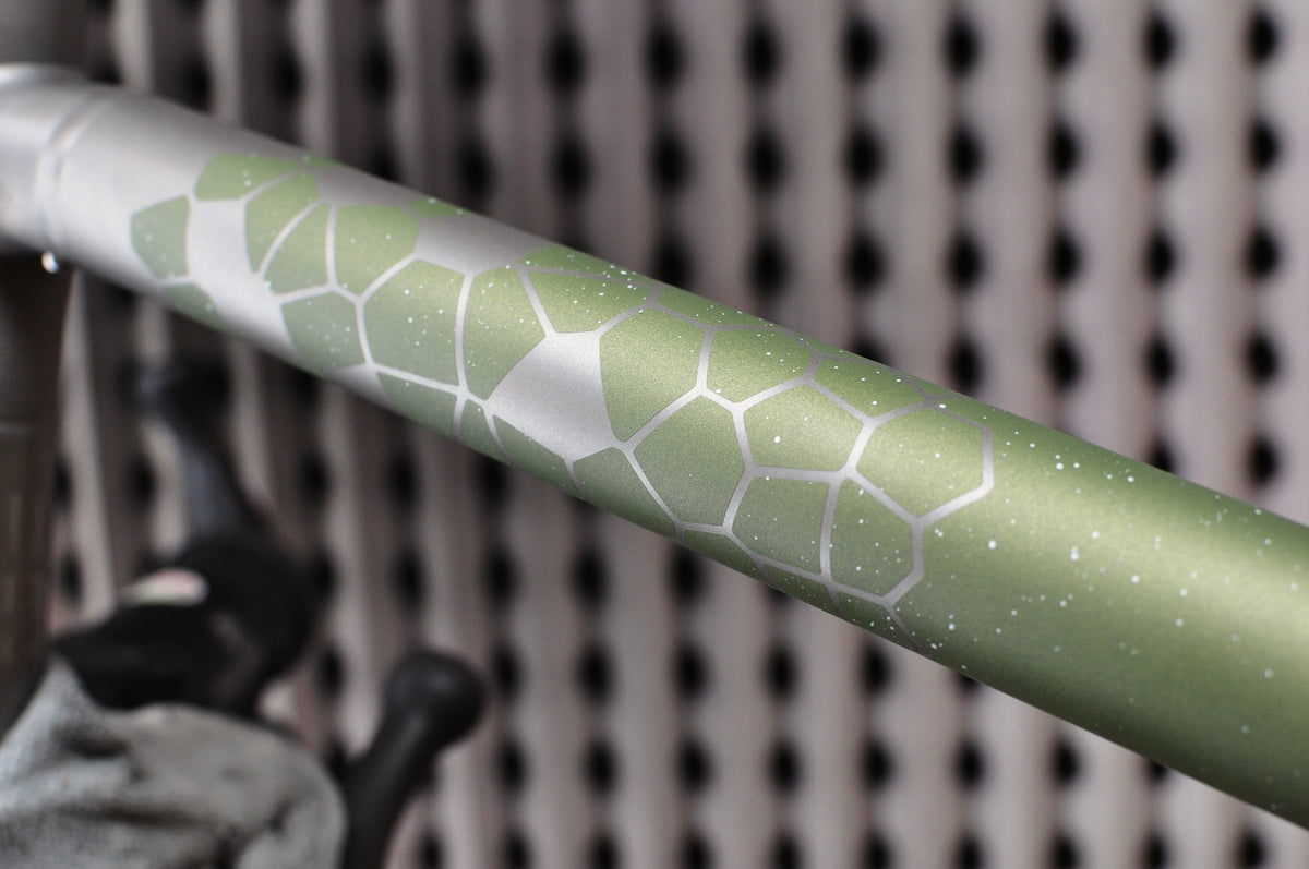 Titanium top tube with olive green speckled paint and a hexagon tortoiseshell pattern