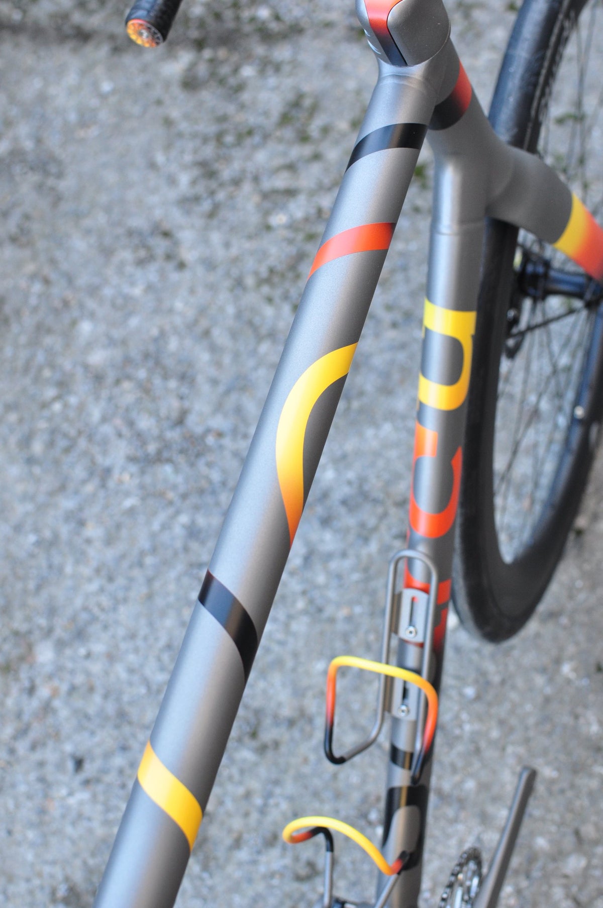 Titanium down tube with yellow, orange and black swirl paint and matching orange-yellow bottle cages