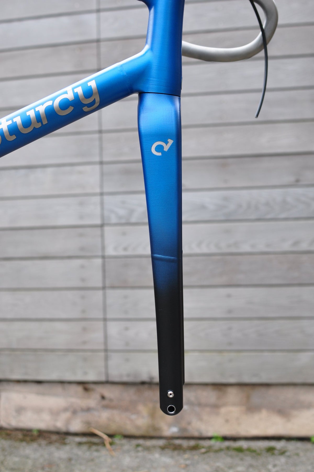 Blue-to-black fade fork and head tube with silver Sturdy logo against a grey timber wall