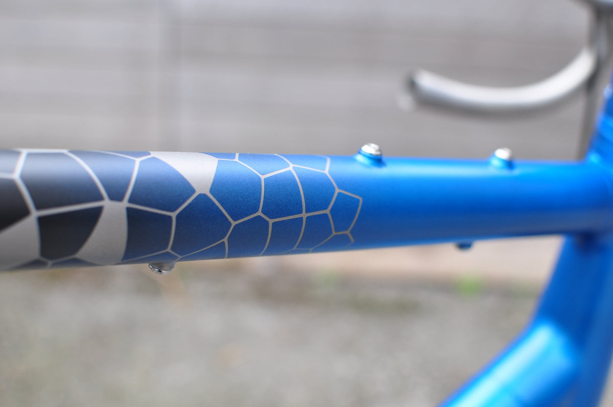 Blue painted top tube with a grey hexagonal cell pattern fading into the paint, close-up