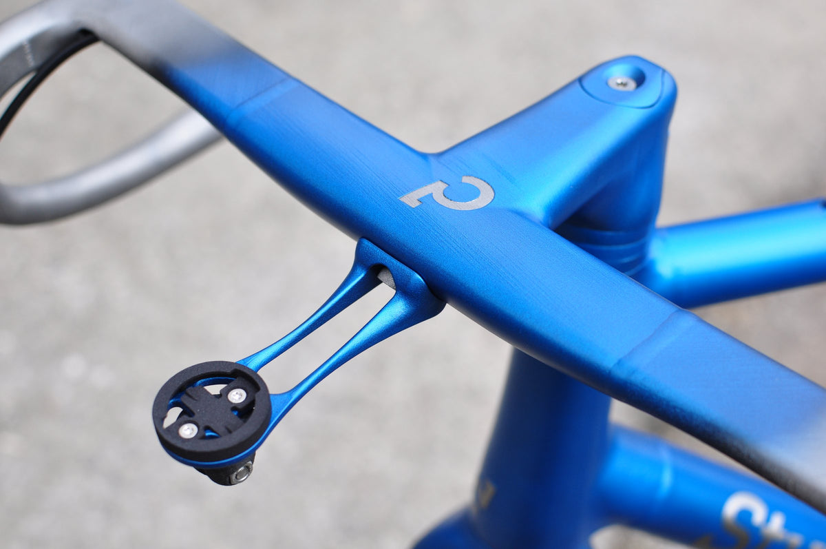 Blue integrated handlebar and stem with silver logo and matching blue computer mount, close-up