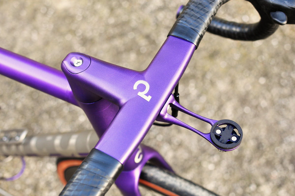 Purple integrated handlebar and stem with white logo and purple computer mount above a gravel yard