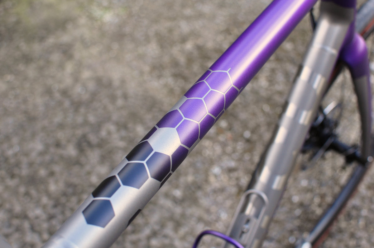 Purple top tube fading into bare titanium through a dark hexagon pattern, close-up