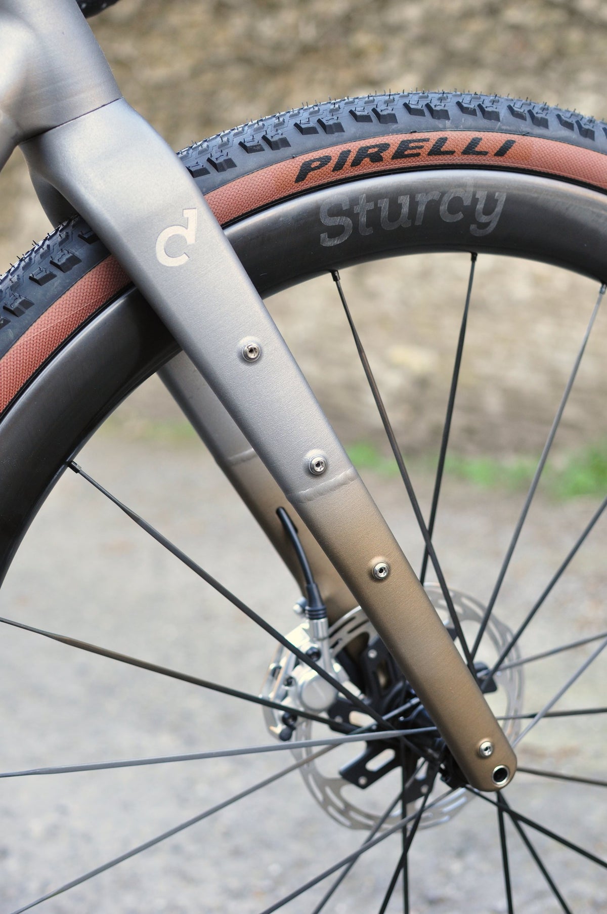 Bare titanium fork with bronze fade at the tip over a Sturdy carbon wheel with tan-wall tyre