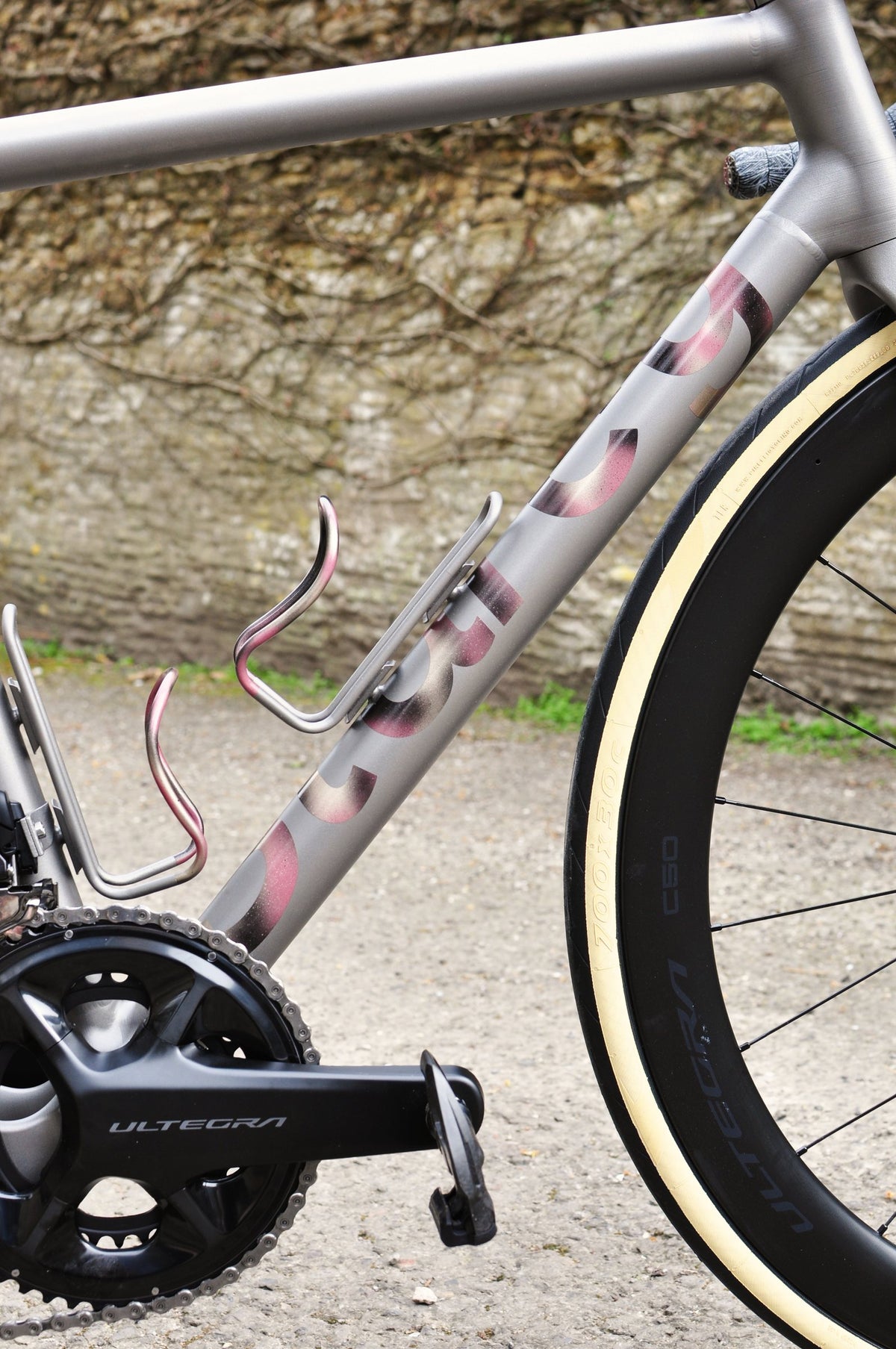 Titanium down tube with pink-to-gold anodised lettering and pink anodised bottle cages by a stone wall