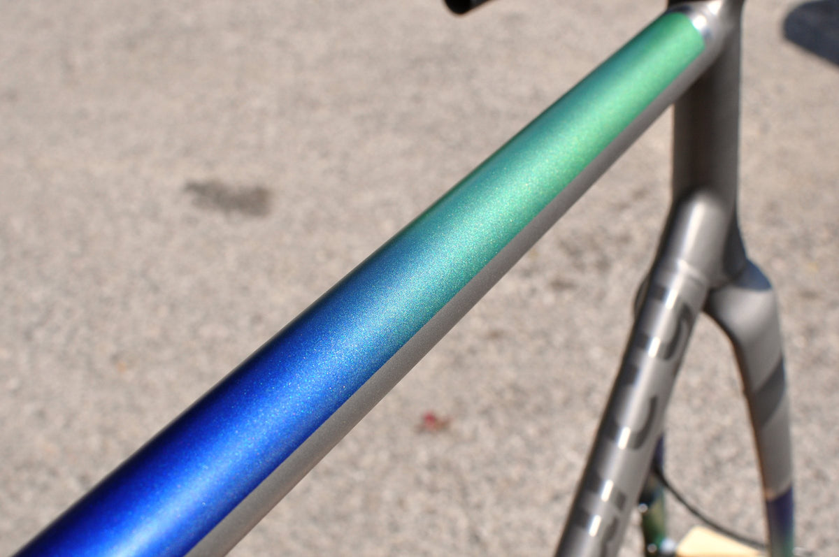 Top tube in sparkling blue-to-green fade paint over bare titanium, close-up
