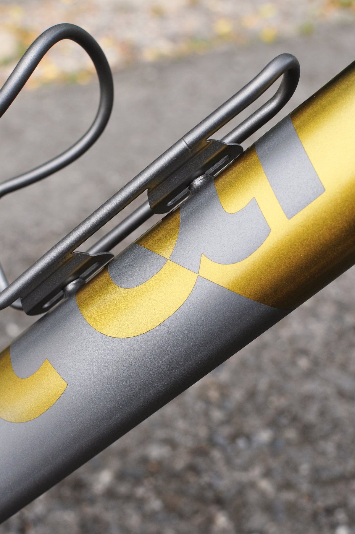 Gold metallic logo lettering on a grey down tube beneath a dark grey bottle cage, close-up