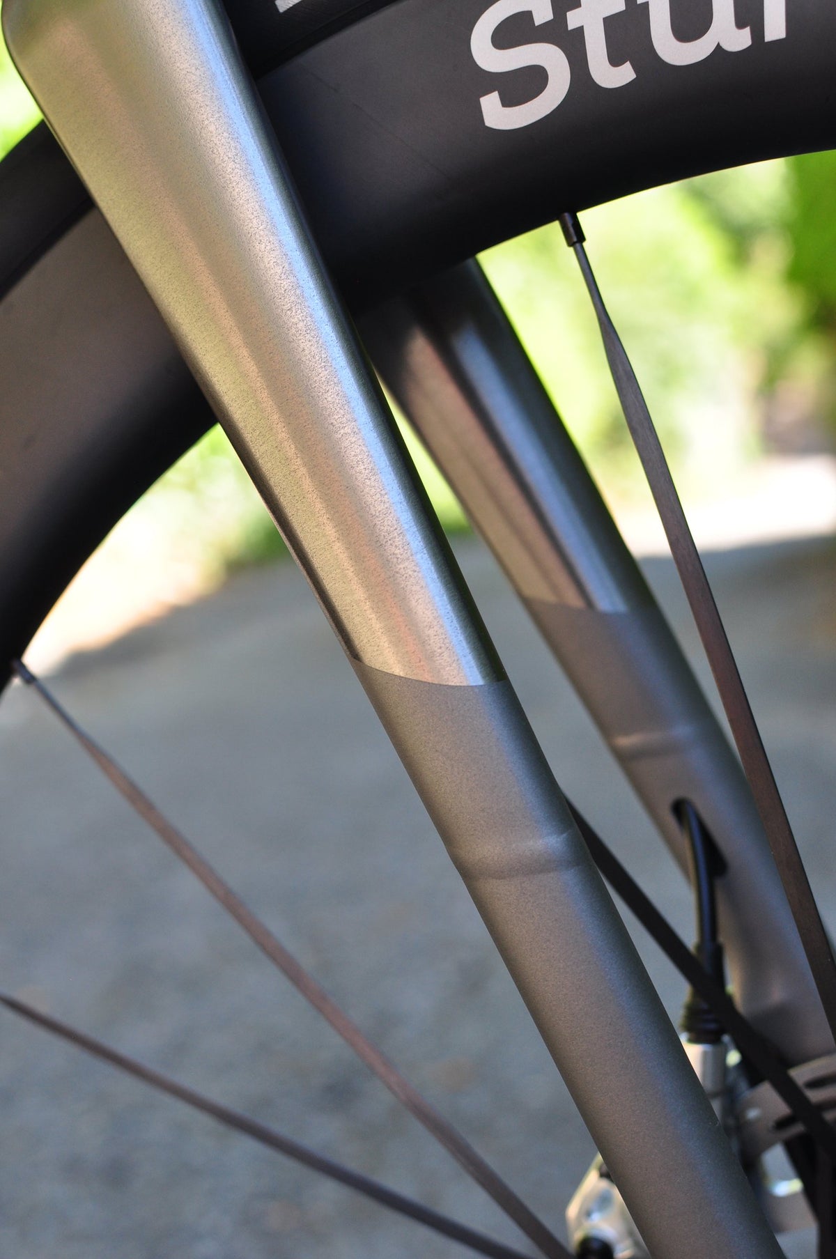 Bare titanium fork with polished and brushed sections in front of a Sturdy carbon wheel