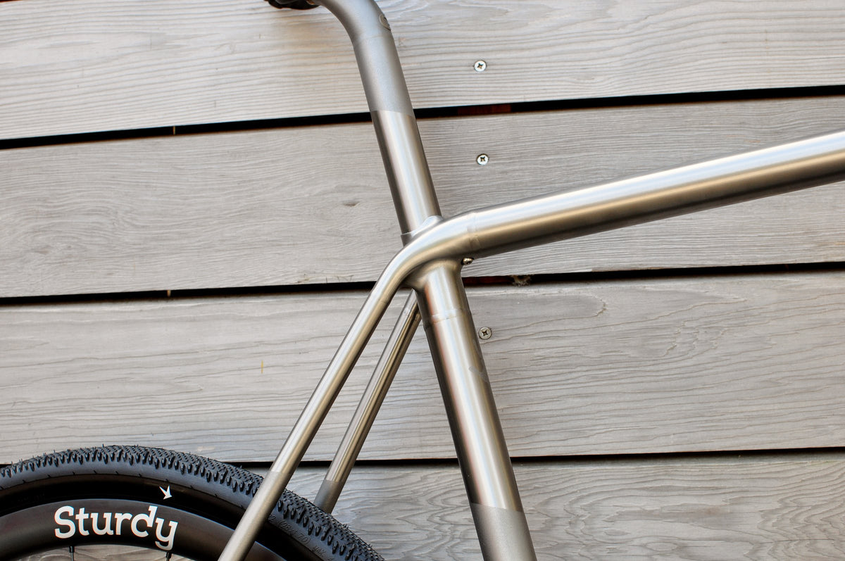 Polished titanium seat cluster and stays with shot-peened bands, Sturdy wheel against grey timber
