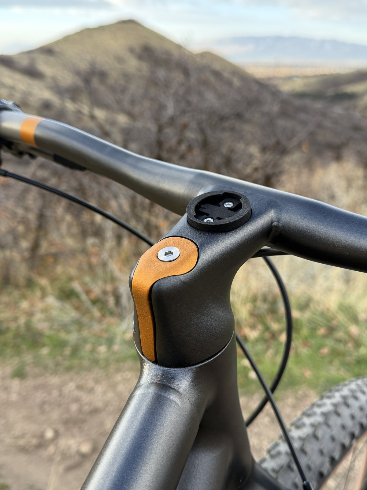 Grey integrated stem and handlebar with copper top cap and computer mount, dry hillside behind