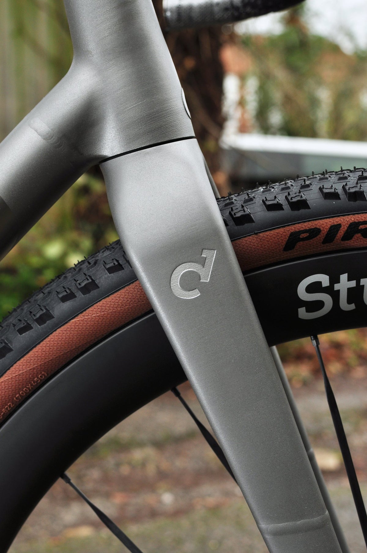 Brushed titanium fork with etched logo beside a knobbly tan-wall tyre on a Sturdy wheel