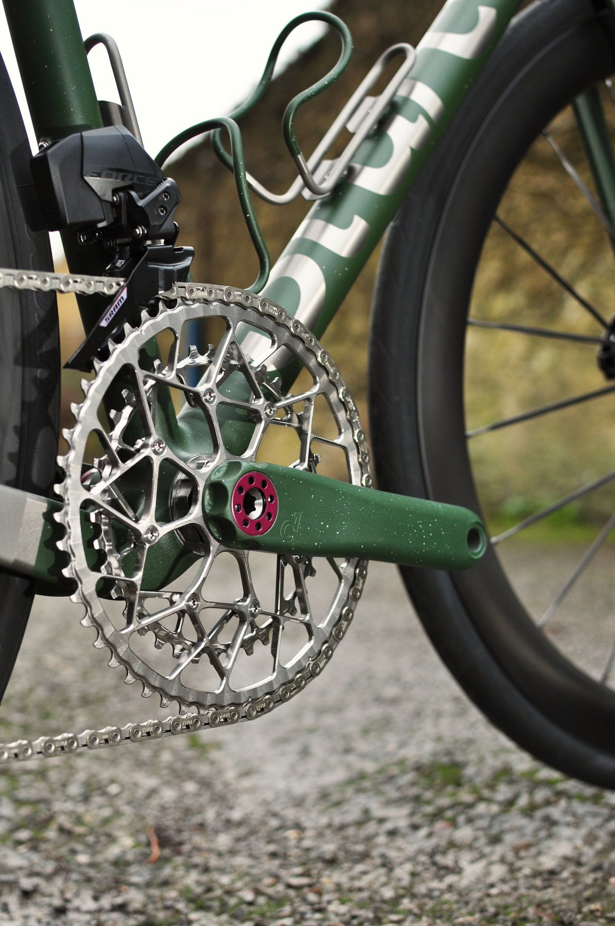 Green speckled crank arm with pink axle bolt and silver chainring on a green and titanium frame