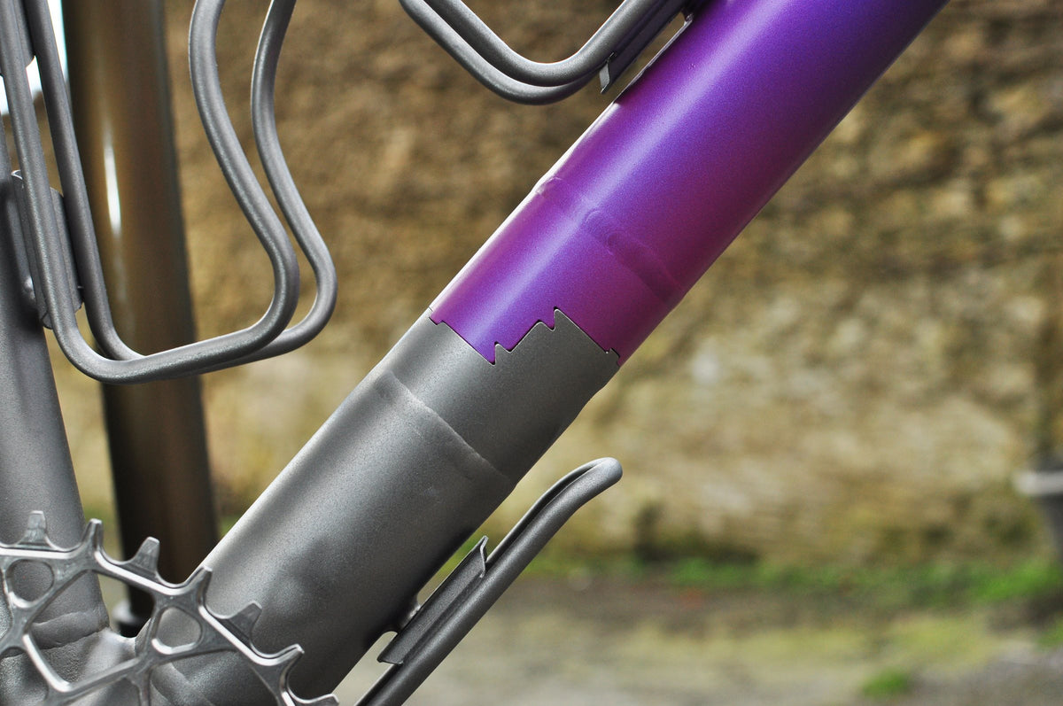 Shot-peened titanium down tube with purple paint and a stepped edge, titanium bottle cages above