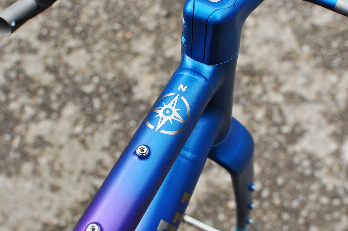 Blue-to-purple painted top tube and head tube with a silver compass rose design
